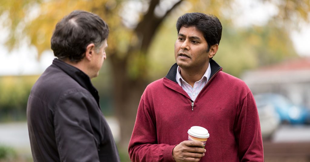 Two men talking to each other, one holding a takeaway coffee cup