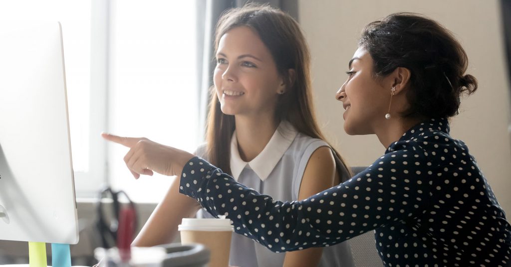 Two women speaking to each other in front of a computer