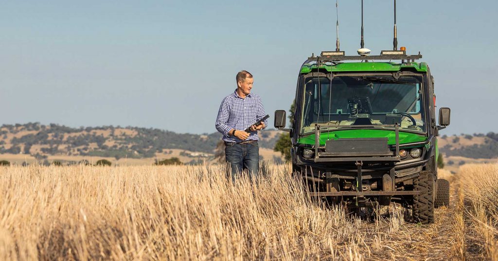 A man stands in a crop field beside a tractor, inspecting crops as part of sustainable agriculture study.