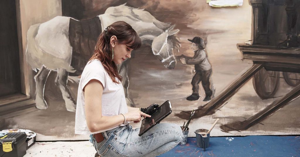 woman on ipad in front of wall painting
